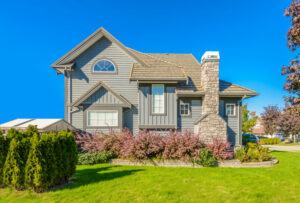 Exterior view of a gray two-story starter home with stone chimney and green lawn.